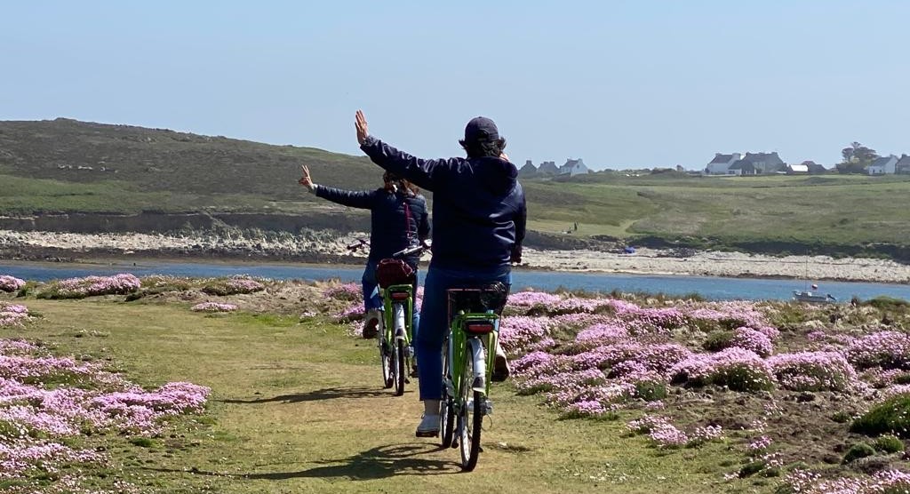 eux cyclistes de dos sur un chemin fleuri au bord de la mer