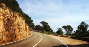 Route de corniche sinueuse longeant une paroi rocheuse orangée, sous un ciel bleu