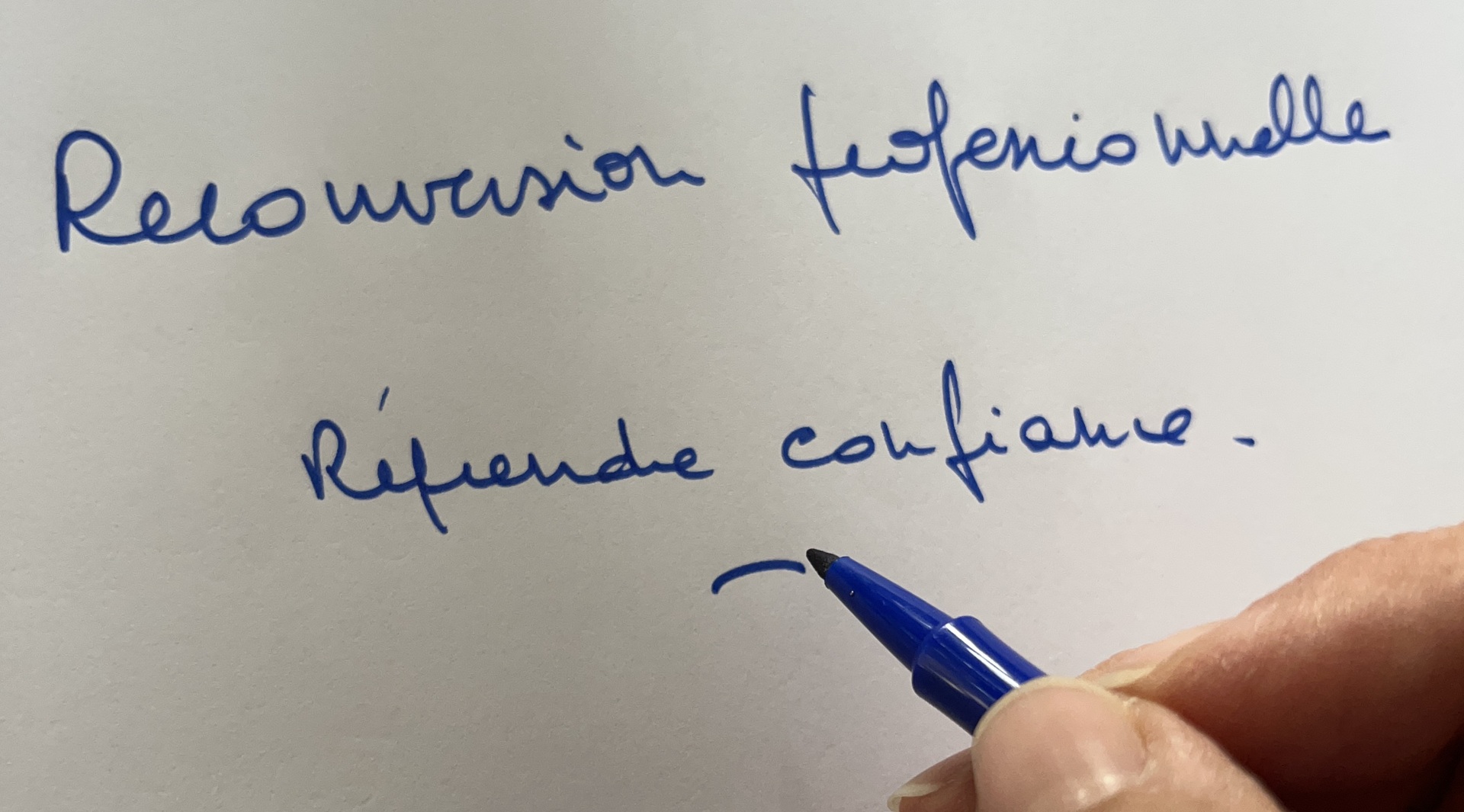 Main écrivant « Reconversion professionnelle, reprendre confiance » au feutre bleu