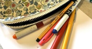Trousse fleurie ouverte avec des stylos de couleur posés sur une feuille blanche
