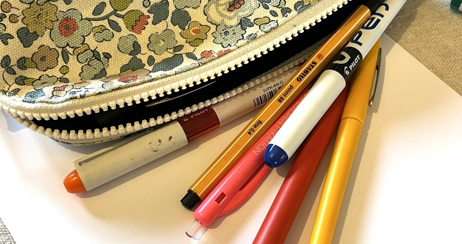 Trousse fleurie ouverte avec des stylos de couleur posés sur une feuille blanche